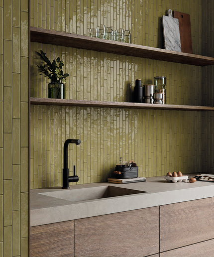 Modern kitchen backsplash with glossy olive green vertical subway tiles, open wood shelves, and black faucet