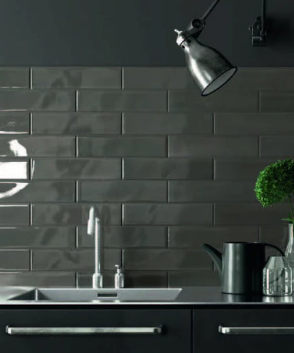 Glossy dark subway tile backsplash in modern kitchen with sink and black fixtures