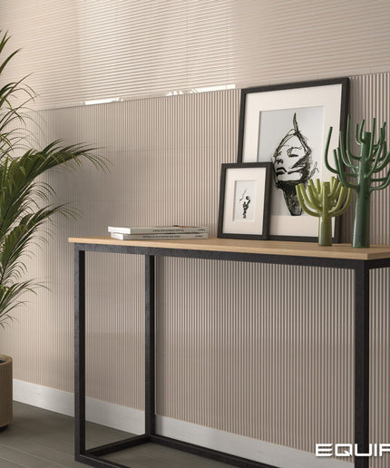 A modern console table with a light wood top and black metal frame, styled in a room setting with framed art, cacti, and a potted plant against a beige ribbed wall.