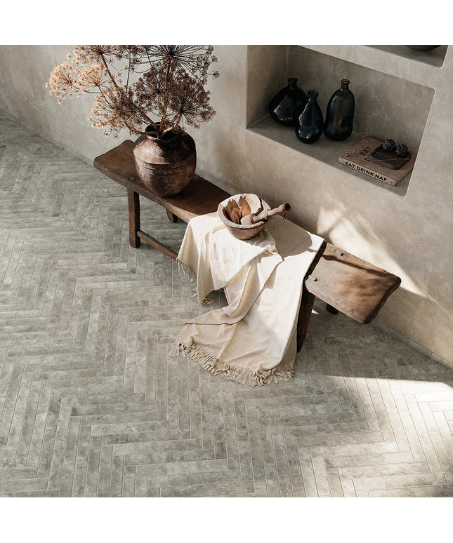 Room interior with wooden bench, vase, and decorative items on a herringbone-patterned floor.
