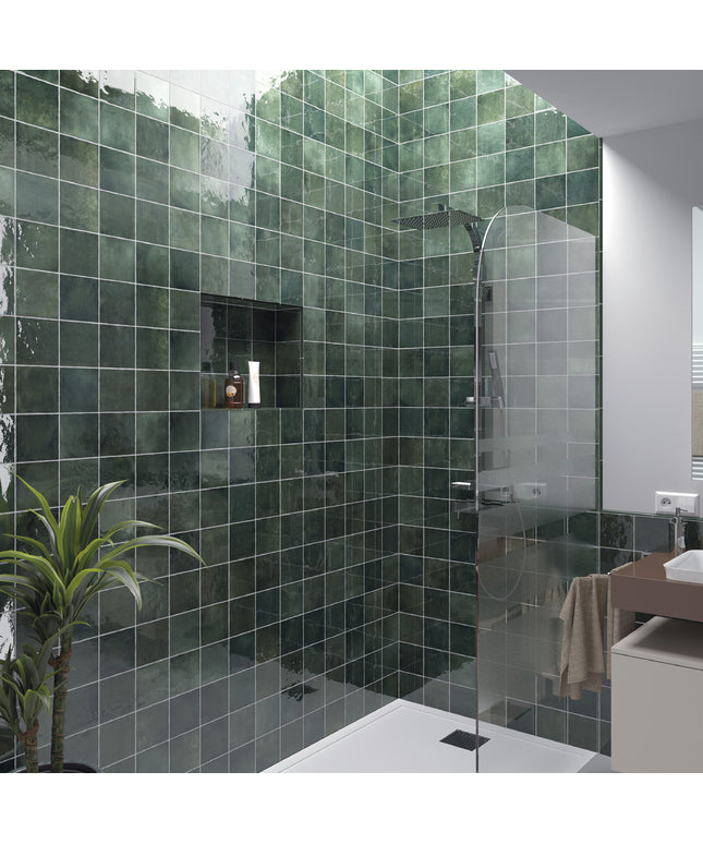 A modern bathroom corner featuring dark green glossy square wall tiles, a glass shower door, a built-in niche shelf, and a small potted plant.