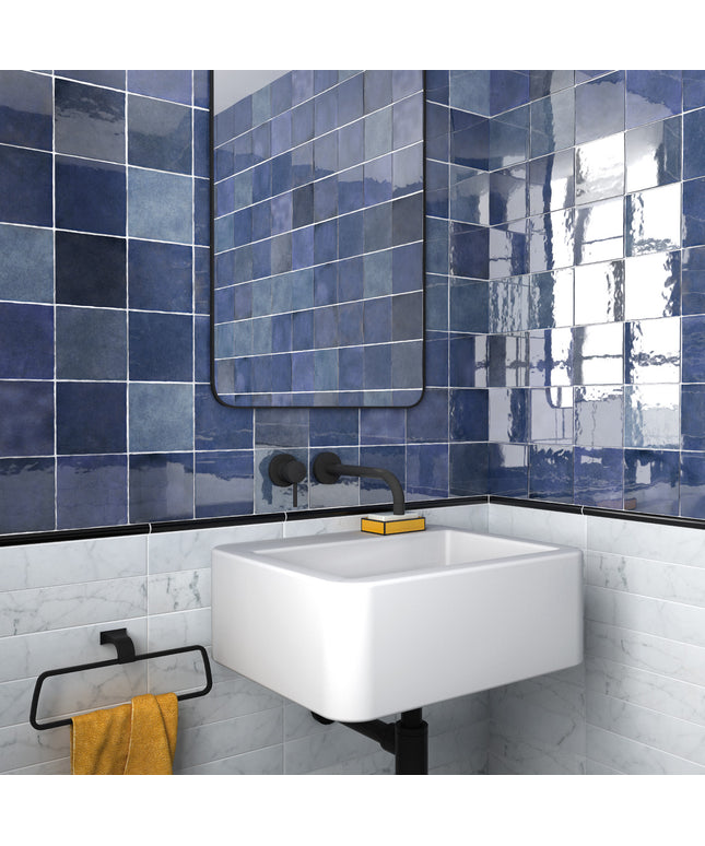 A modern bathroom corner featuring glossy blue square wall tiles, a white floating sink, a black faucet, and a yellow towel on a black rack.