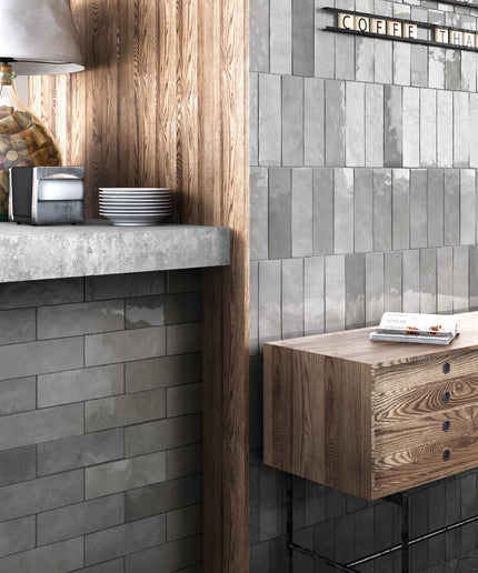 Gray rectangular subway wall tiles installed in a modern kitchen or cafe setting, shown alongside a wooden counter, a glass jar lamp, and a small wooden cabinet.