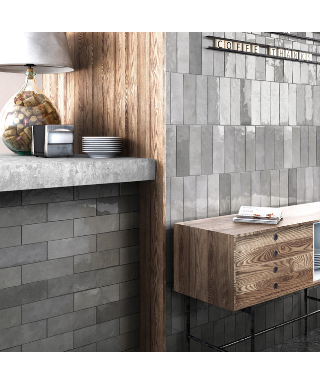 Gray rectangular subway wall tiles installed in a modern kitchen or cafe setting, shown alongside a wooden counter, a glass jar lamp, and a small wooden cabinet.