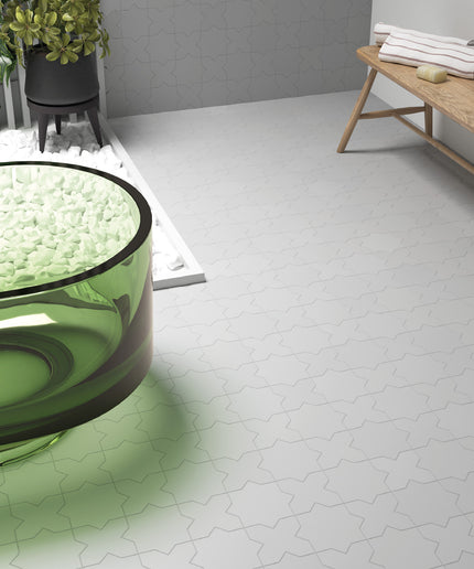 White hexagonal floor tiles with a subtle gray outline pattern, shown in a modern bathroom setting alongside a green glass tub, a wooden bench, and potted plants.