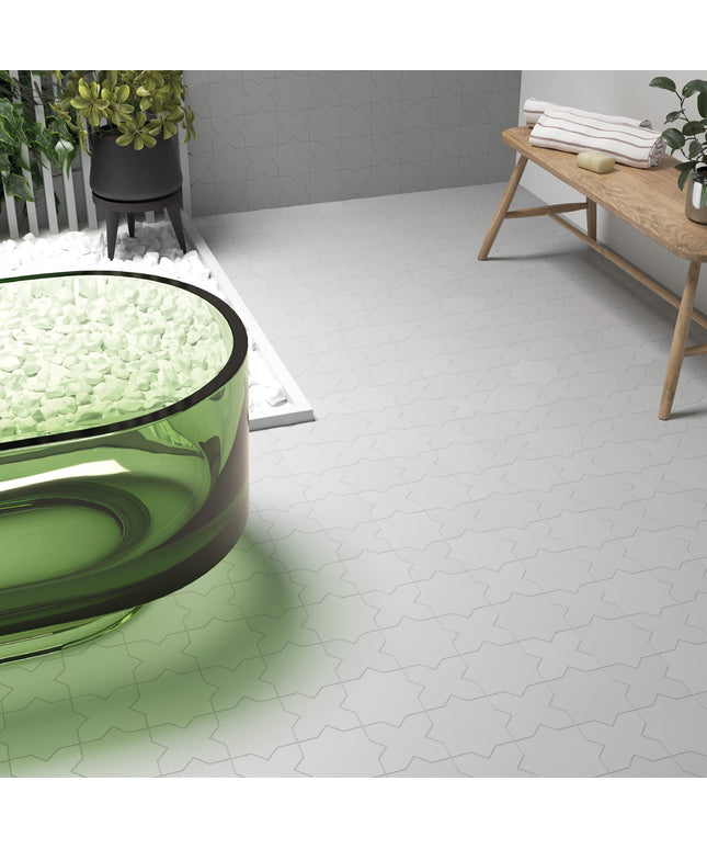 White hexagonal floor tiles with a subtle gray outline pattern, shown in a modern bathroom setting alongside a green glass tub, a wooden bench, and potted plants.