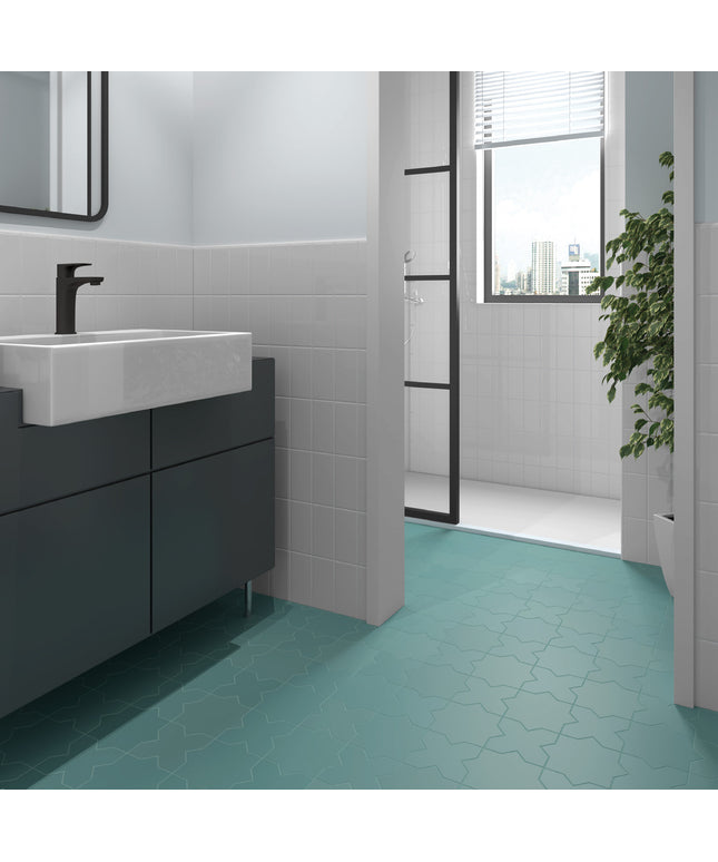 A modern bathroom interior featuring a teal geometric mosaic floor tile, a white rectangular vessel sink, a dark gray floating vanity, and a glass shower door in the background.