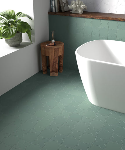 Bathroom with green tiled floor, white freestanding bathtub, and wooden stool.