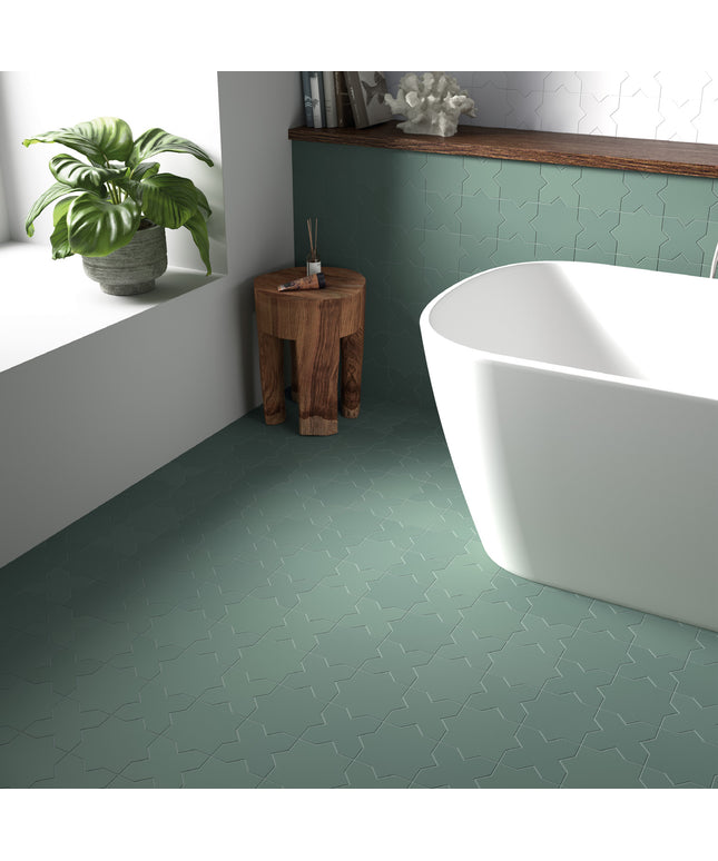 Bathroom with green tiled floor, white freestanding bathtub, and wooden stool.