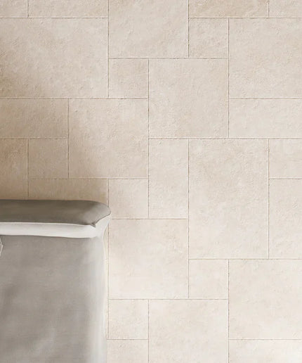Beige tiles with a herringbone pattern on a wall with a gray bench.