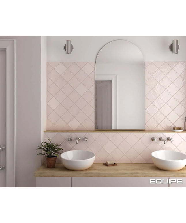 A modern bathroom vanity setup featuring a light pink diamond-patterned tiled backsplash, a large arched mirror, a light wood countertop, and two white ceramic vessel sinks. The image is branded with 'EQUIPE' in the bottom right corner.