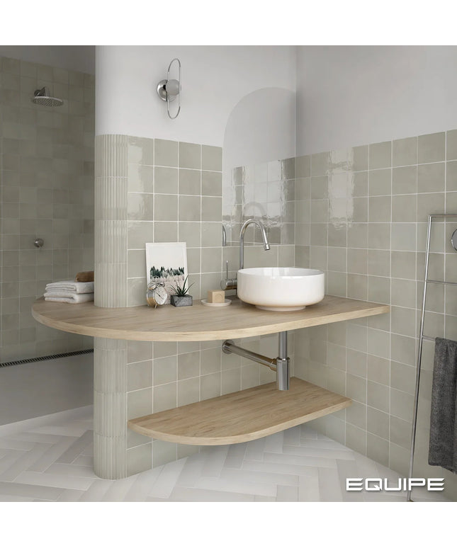 A modern floating bathroom vanity with a curved light wood top and lower shelf, a white vessel sink, and a chrome faucet, set against beige tiled walls.