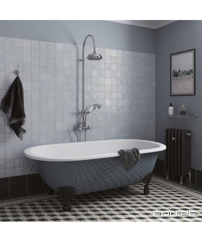 A freestanding clawfoot bathtub in a blue-gray finish with a white interior, set in a styled bathroom with light blue tiled walls, a chrome shower fixture, and a black patterned floor.