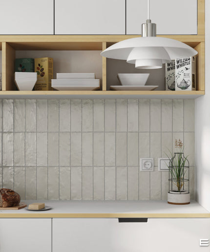 A modern kitchen interior featuring a textured light gray tile backsplash, light wood open shelving with white dishes, a white pendant light, and a stainless steel refrigerator. The word 'EQUIPE' appears in the bottom right corner.