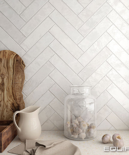 Decorative setting with a pitcher, jar, and wooden board against a herringbone tiled wall.