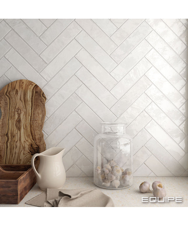 Decorative setting with a pitcher, jar, and wooden board against a herringbone tiled wall.