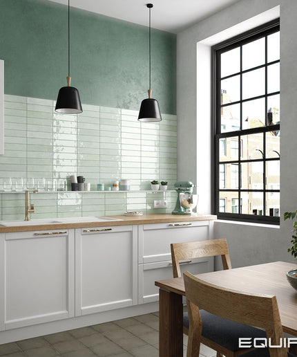 Modern kitchen with green tiled wall, white cabinets, and a dining area.