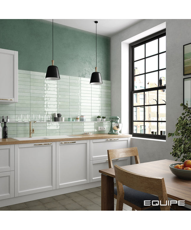 Modern kitchen with green tiled wall, white cabinets, and a dining area.