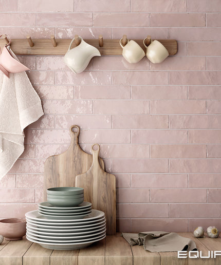Kitchen setting with pink tiled wall, wooden rack with mugs, and stacked plates on a wooden surface.