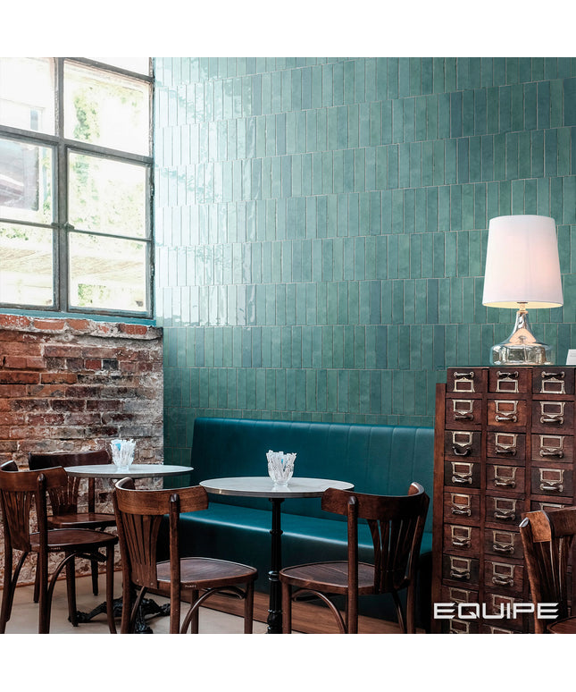 Restaurant interior with teal tiled walls, wooden chairs, and a lamp.