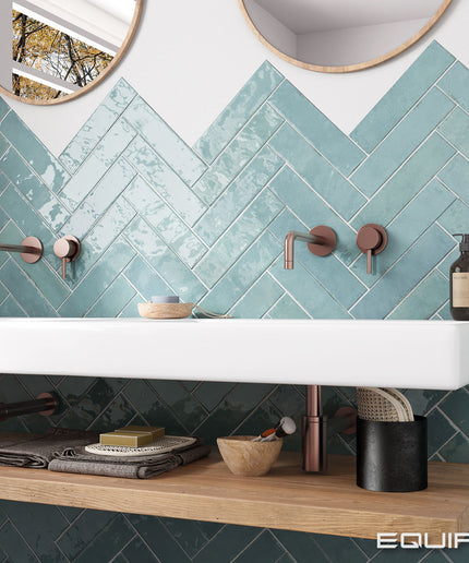 Bathroom with teal herringbone tiles, white sink, and wooden shelf.