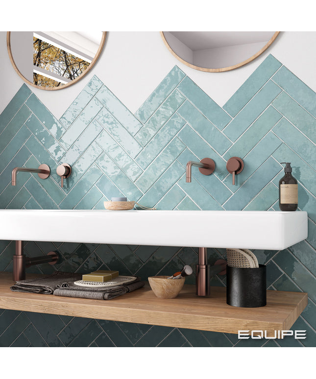 Bathroom with teal herringbone tiles, white sink, and wooden shelf.