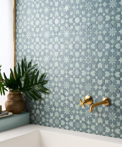 Bathroom corner with geometric patterned tiles, gold faucet, and plant