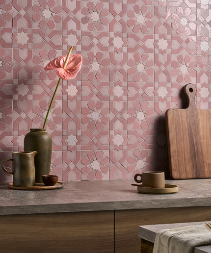 Decorative pink and gray tiled wall with a wooden cutting board, ceramic cups, and a vase.