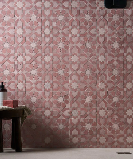 Patterned pink tiles with a small stool and bottle against a wall.