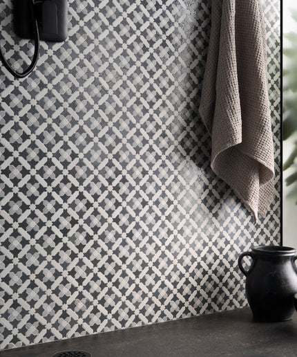 Patterned wall tiles in a bathroom setting with a towel and decorative pot.
