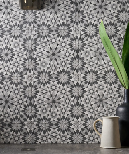 Decorative tiled wall with geometric pattern, a white pitcher, and a black vase with green leaves.