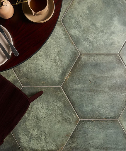 Hexagonal tiles with a rustic finish on a floor, with a table and cutlery in the foreground.