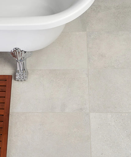 Close-up of a tiled bathroom floor with a white bathtub and wooden shelf.