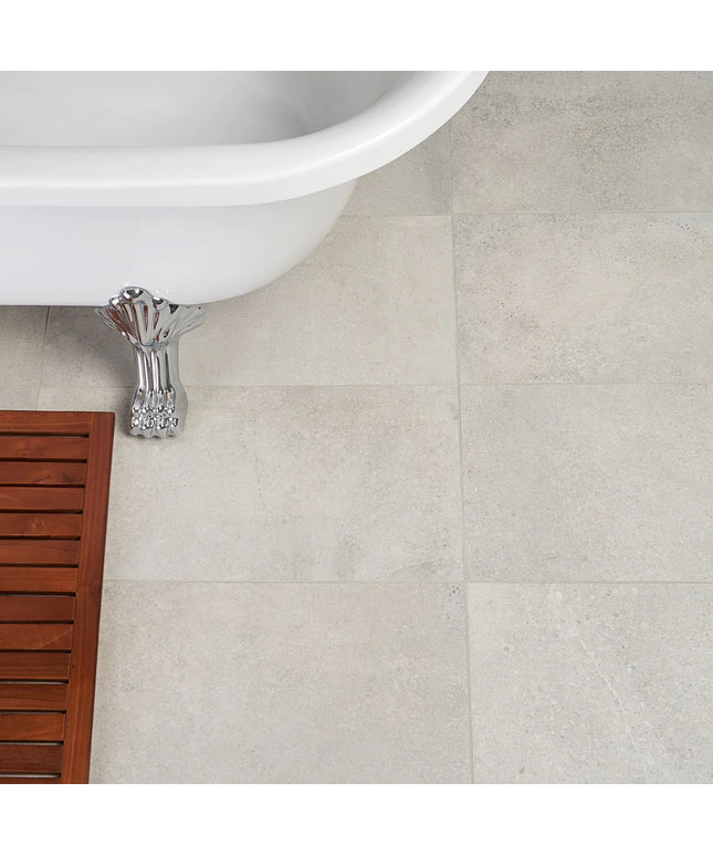 Close-up of a tiled bathroom floor with a white bathtub and wooden shelf.