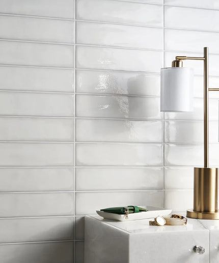 Glossy white rectangular wall tiles in a modern interior with a gold table lamp.