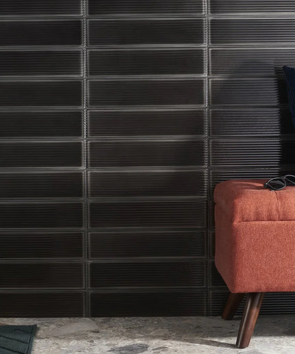 Glossy black fluted 4x16 wall tiles behind a rust bench and navy pillow, modern decor