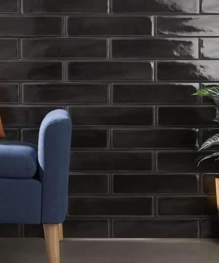 Glossy black subway tiles on wall, with blue sofa and potted plant in modern living room.