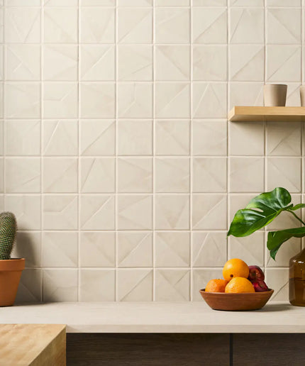 Beige tiled wall with a shelf holding a bowl of fruit, a cactus, and a vase.
