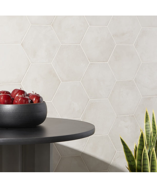 Hexagonal tiles on a wall with a bowl of apples and a plant on a table.
