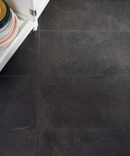 Dark gray tiles on a floor with a white cabinet and colorful plates in the background.