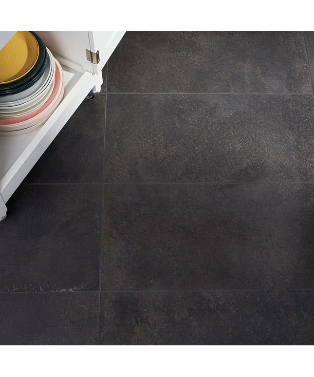Dark gray tiles on a floor with a white cabinet and colorful plates in the background.