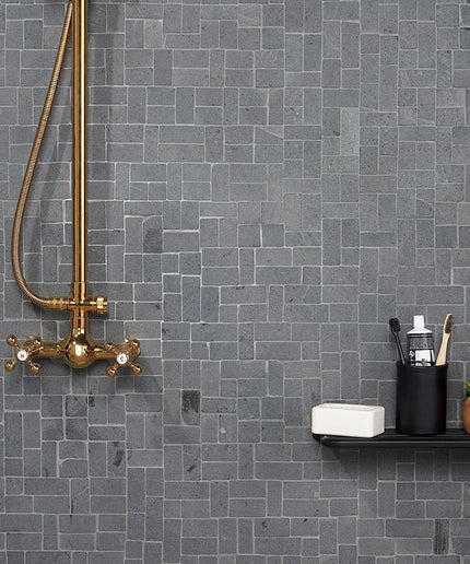 Black lava natural stone mosaic tile wall in modern bathroom with brass shower fixture