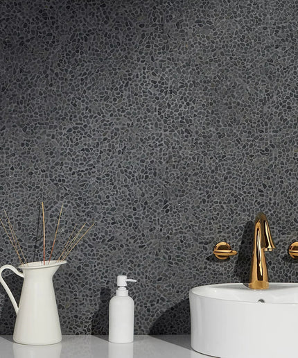 Black lava wall tiles with textured pebble pattern behind modern bathroom sink and gold faucet