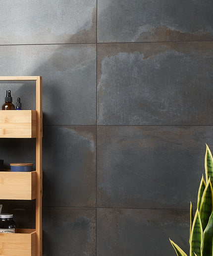 Bathroom setting with wooden shelf against a gray tiled wall, featuring a plant on the right.