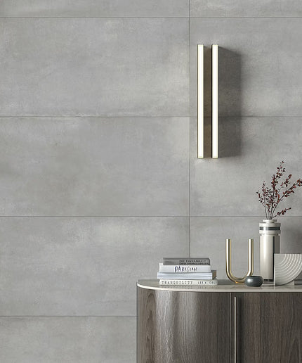 Modern bathroom setting with a wall-mounted light fixture, books, and decorative items against a gray tiled wall.