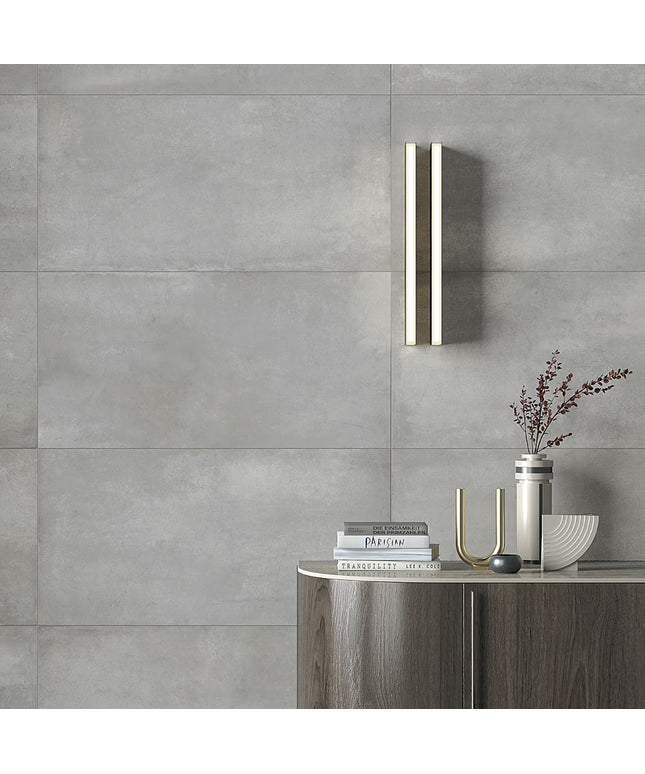 Modern bathroom setting with a wall-mounted light fixture, books, and decorative items against a gray tiled wall.