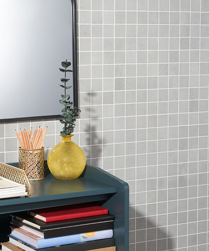 Gray tiled wall with a shelf holding books, a yellow vase, and pencils.