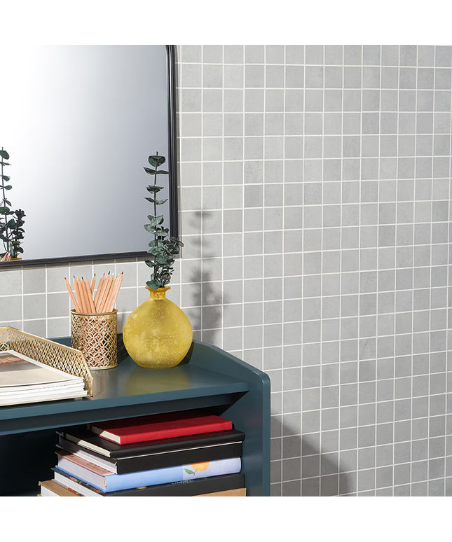 Gray tiled wall with a shelf holding books, a yellow vase, and pencils.