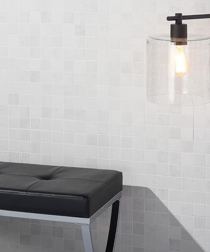 Modern black floor lamp with clear glass shade against a white tiled wall.