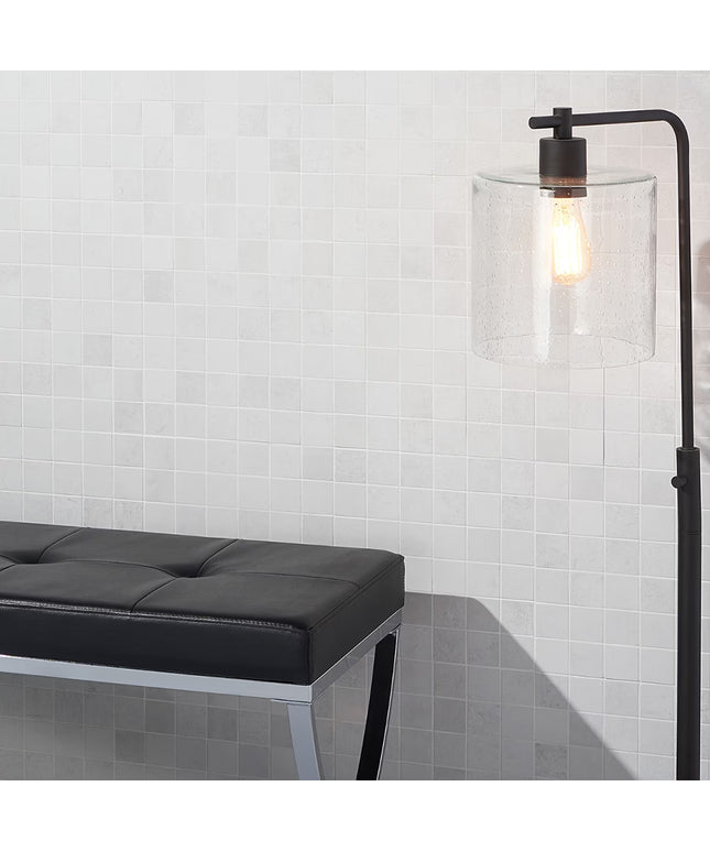 Modern black floor lamp with clear glass shade against a white tiled wall.